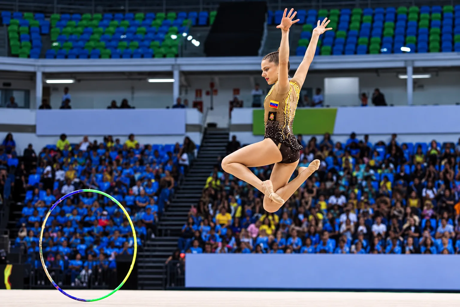 A gymnast alone on the competition carpet, mid-leap during her hoop routine, with the arena crowd behind her