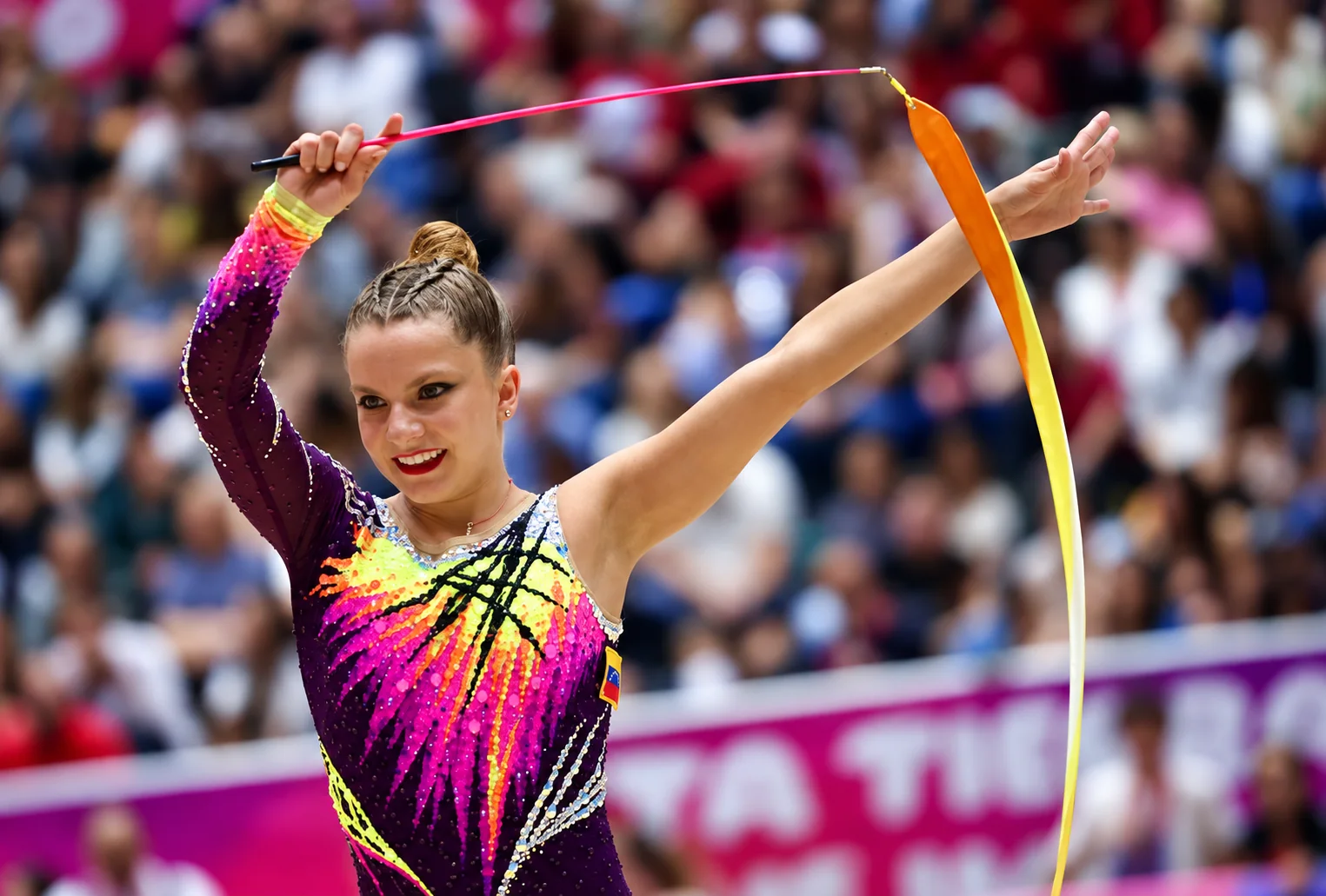 Smiling rhythmic gymnast raising both arms as her ribbon circles above her