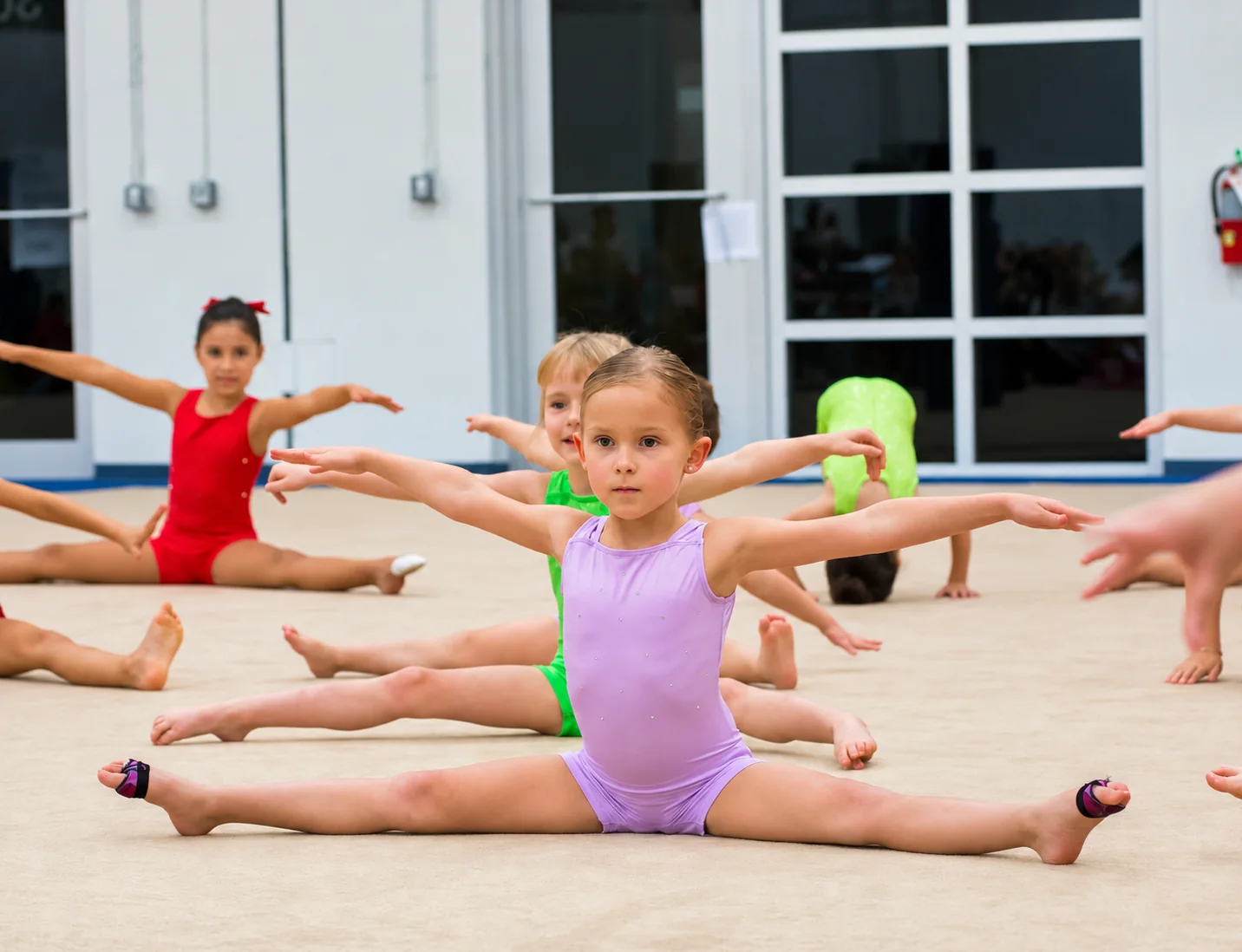 Young Rhythmic Art athletes practicing splits and arm positions during a group class