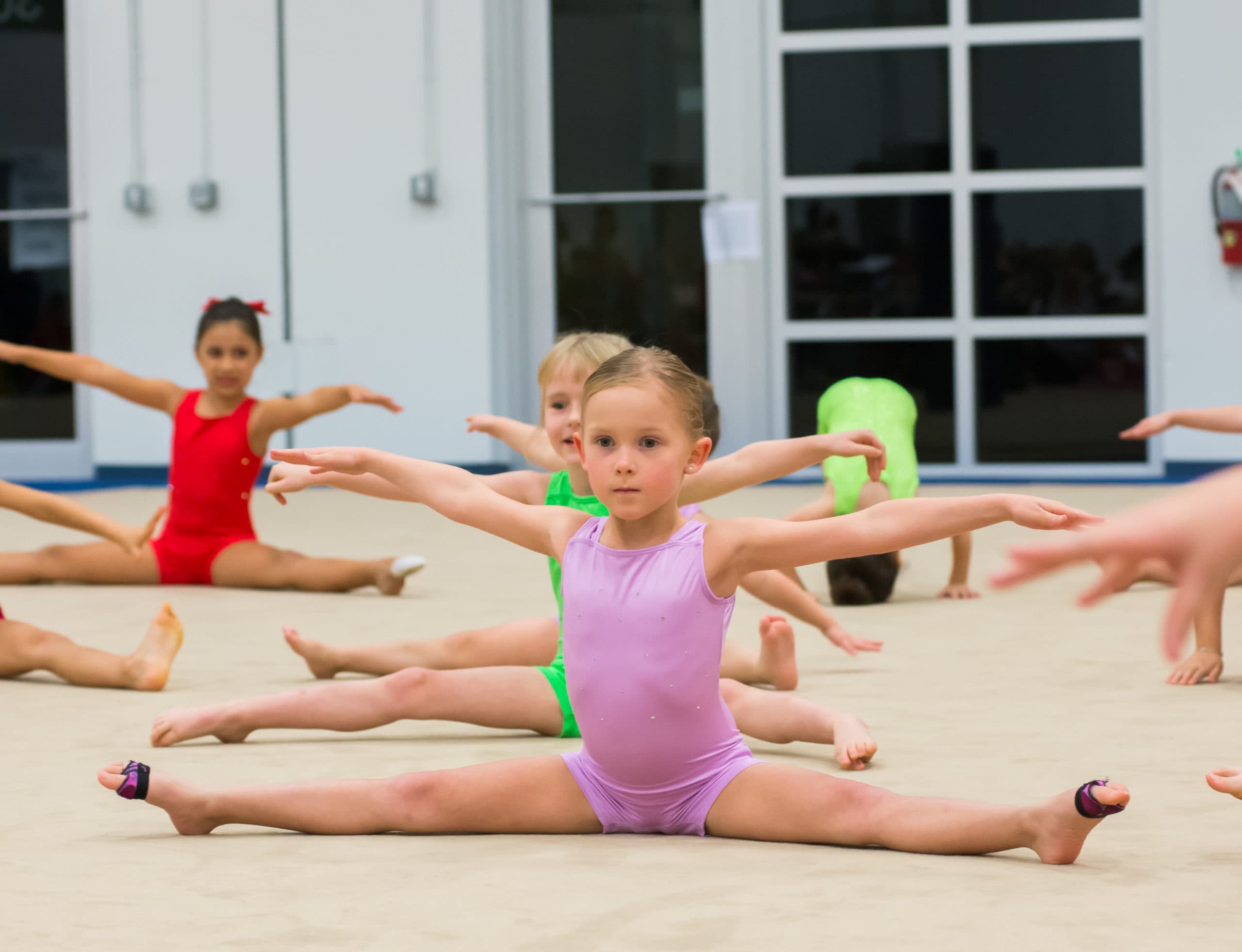 Young Rhythmic Art athletes practicing splits and arm positions during a group class