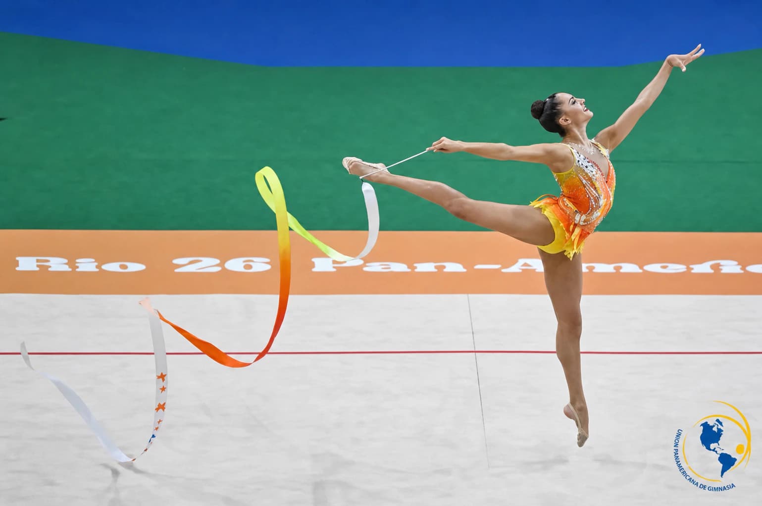 Rhythmic gymnast performing a split leap with a ribbon on a competition floor