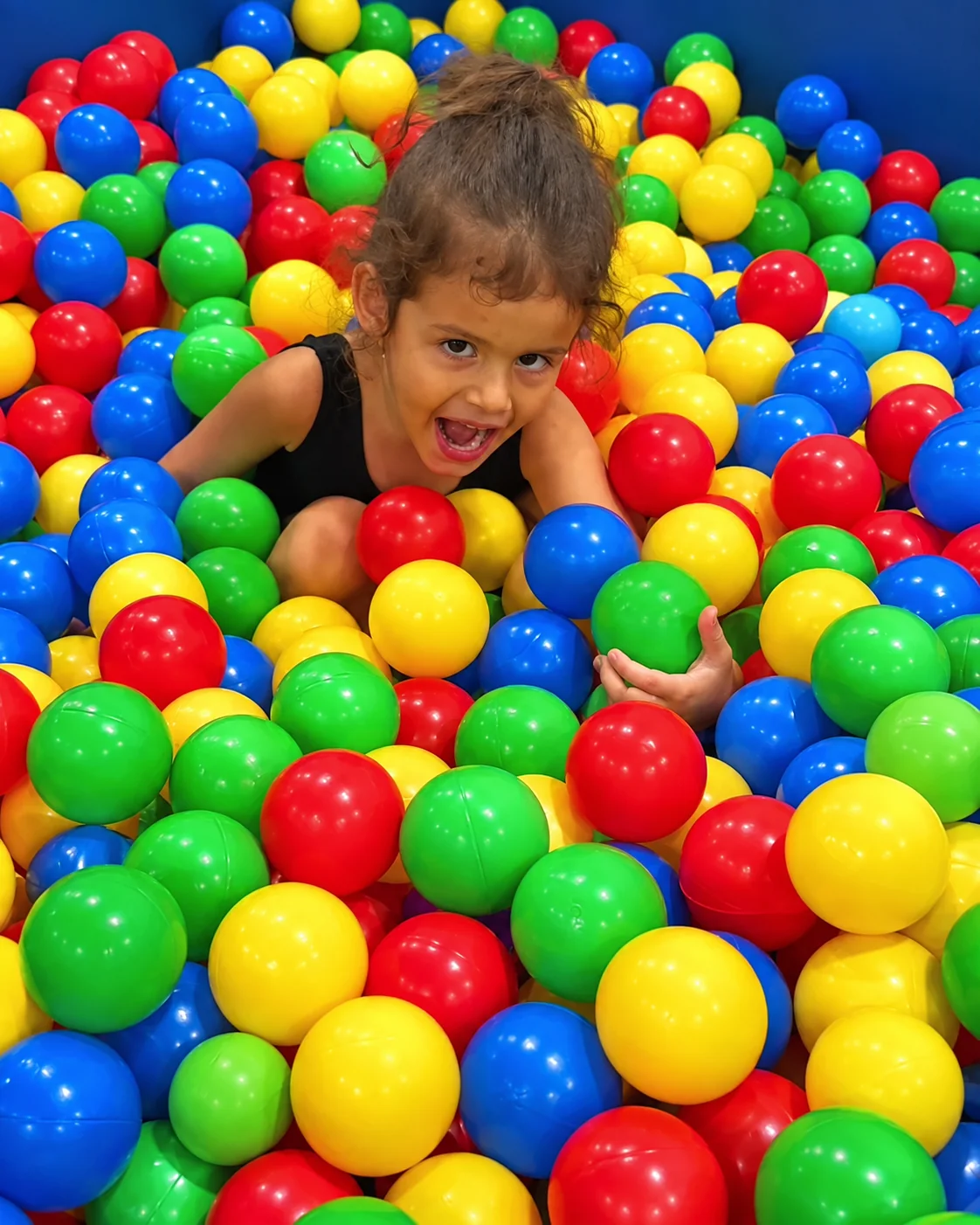 A child playing among colorful balls in the ball pit during a toddler class at Rhythmic Art