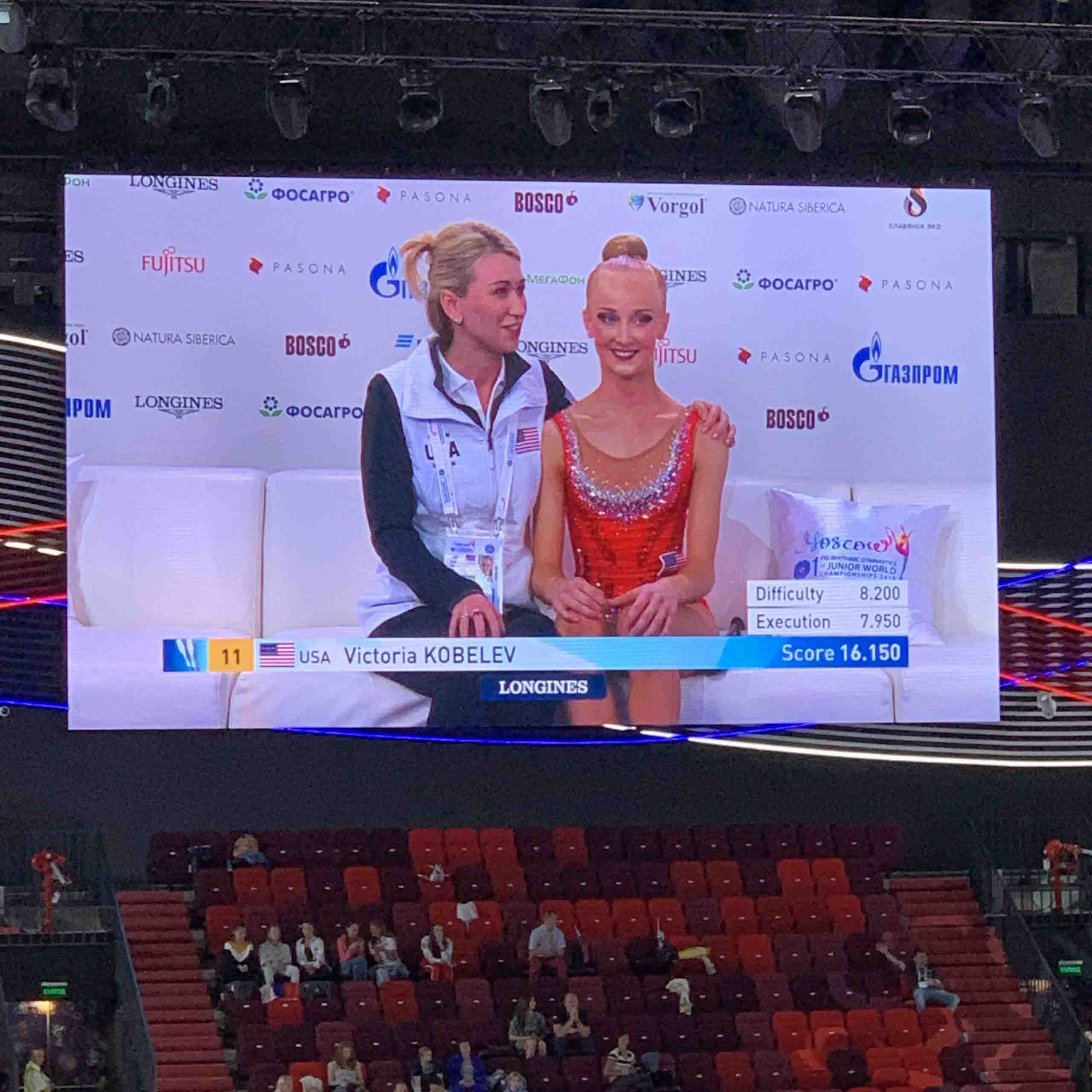 A Rhythmic Art coach and athlete shown on the event screen after a rhythmic gymnastics performance