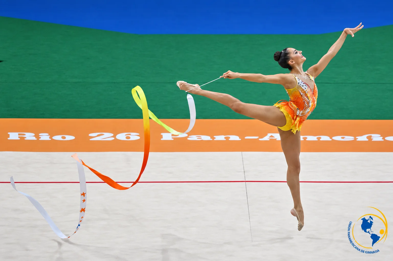 Gimnasta rítmica realizando un salto en split con cinta sobre una pista de competencia