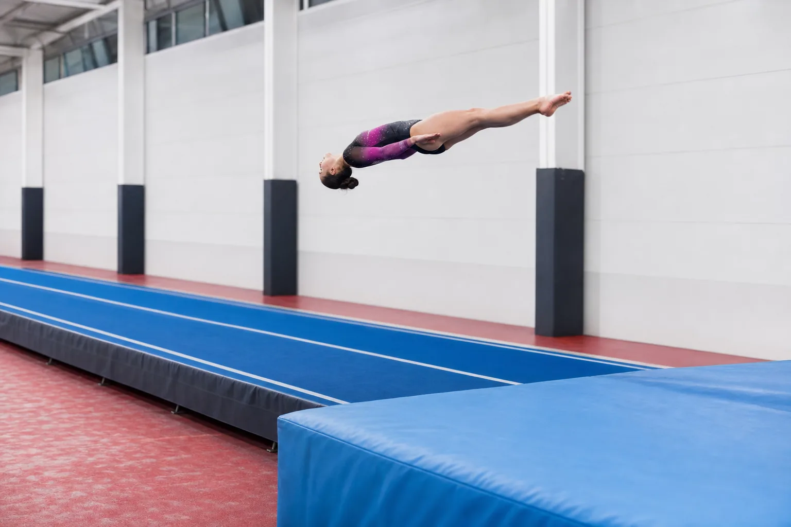 Gymnast performing a straight-body backward flip above a long sprung tumbling track