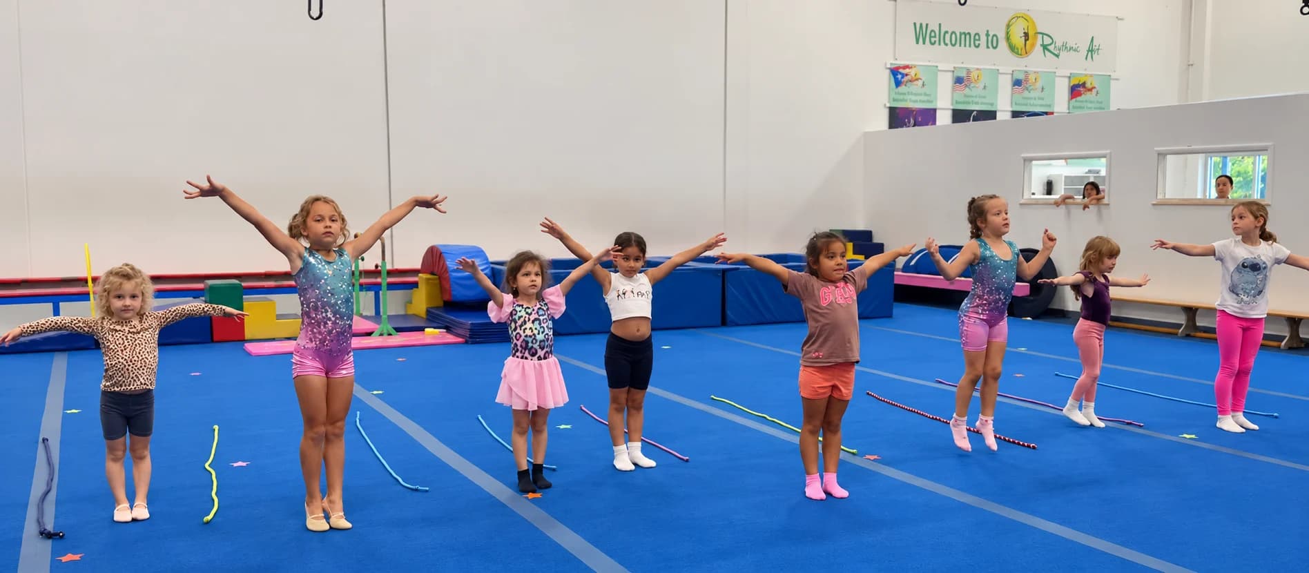 A row of young gymnasts raising their arms during a class in the Blue Gym at Rhythmic Art
