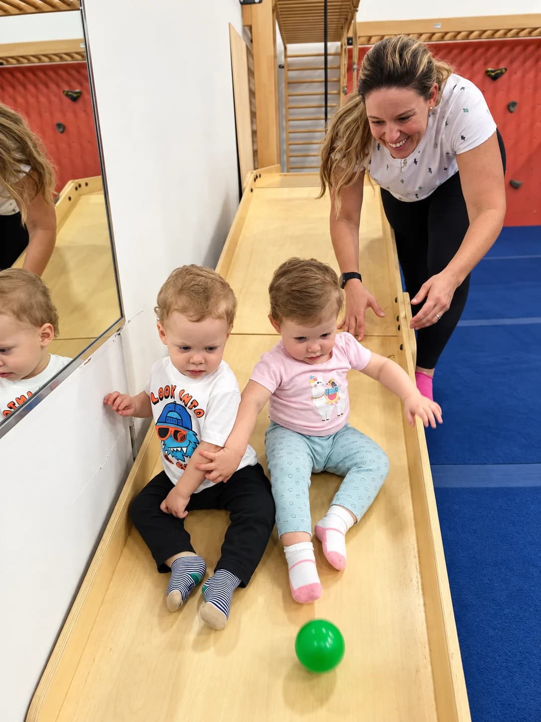 A smiling adult cheering two toddlers on a slide at Rhythmic Art