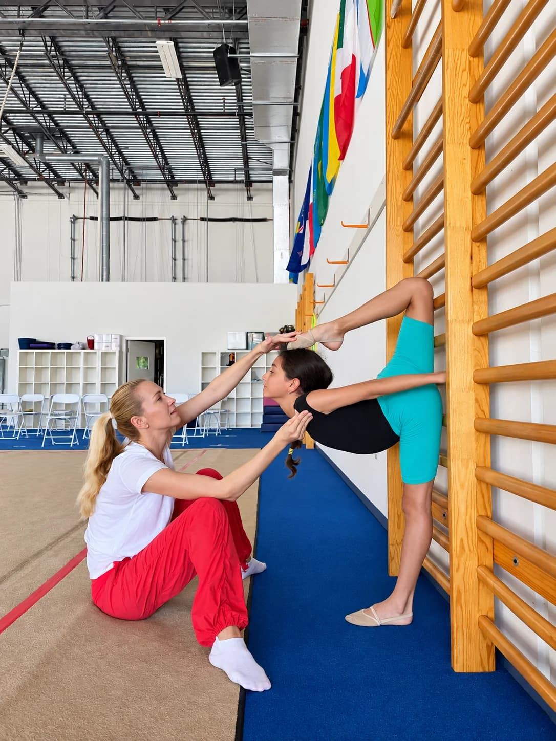 Rhythmic Art coach assisting an athlete with a stretching exercise at the wall bars