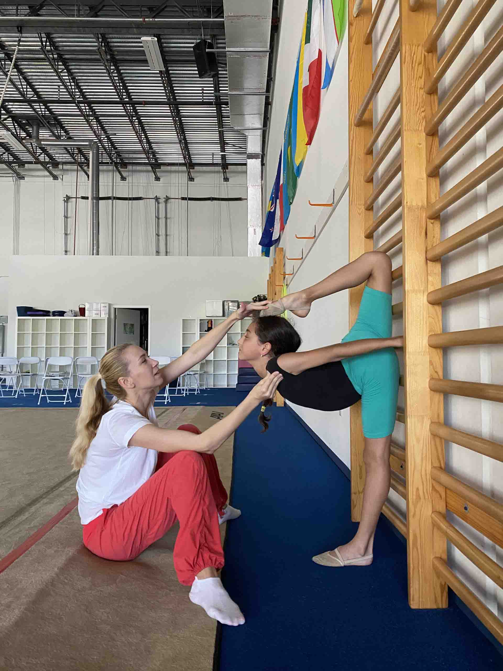 Rhythmic Art coach assisting an athlete with a stretching exercise at the wall bars